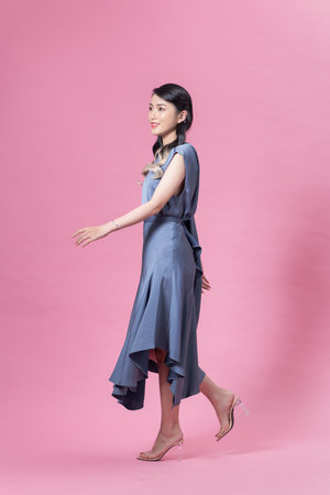 Young woman in blue dress and high heels is walking on pink backgroundの写真素材