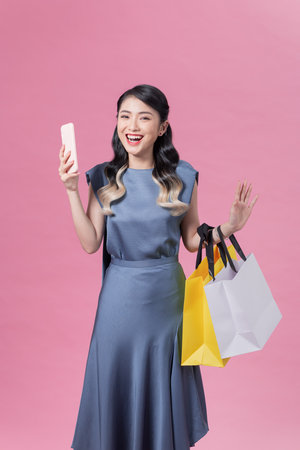 Incredibly excited young woman holding smartphone and shopping bags looking at camera in surpriseの写真素材