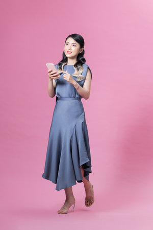 Pretty woman holding smartphone and browsing internet or chatting isolated over pink background in studioの写真素材
