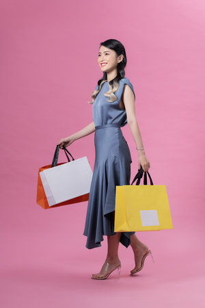 Full Body portrait of beautiful happy woman with bags isolated on pink. Shopping concept.の写真素材