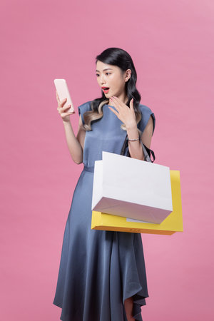Shocked and excited shopping woman using app on smartphone on pink isolated backgroundの写真素材