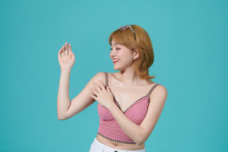 Smiling woman touching her arms while standing against a cyan backgroundの写真素材