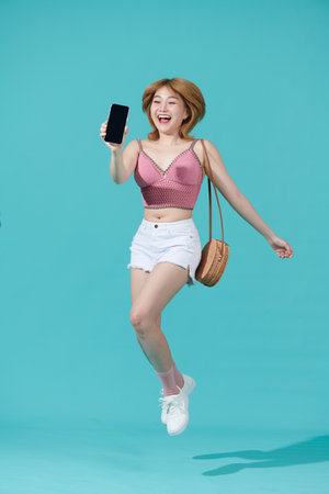 Portrait of beautiful young asian girl jumping up, isolated on cyan backgroundの写真素材