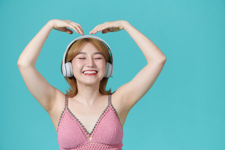 Pretty Asian girl got carried away with music holds smartphone enjoys favorite playlist via headphones has relaxed carefree expressionの写真素材