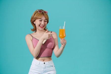 Excited happy young woman enjoys a cool cocktail laughing and having fun isolated on turquoise party summer backgroundの写真素材