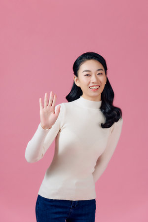 Friendly, pleasant and cheerful east-asian woman raising palm, wave hand greeting and smiling on pink backgroundの写真素材