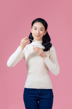 young beautiful smiling woman eating fresh yogurt on pink