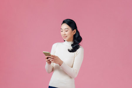 Happy casual woman using smartphone over pink backgroundの写真素材