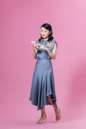 Pretty woman holding smartphone and browsing internet or chatting isolated over pink background in studioの写真素材