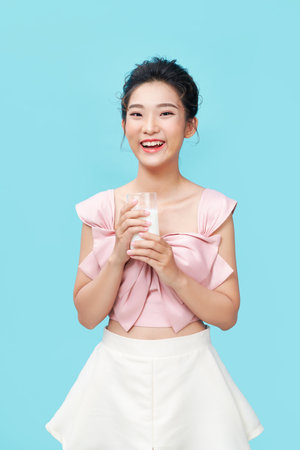 Beautiful young woman with glass of milk over cyan backgroundの写真素材
