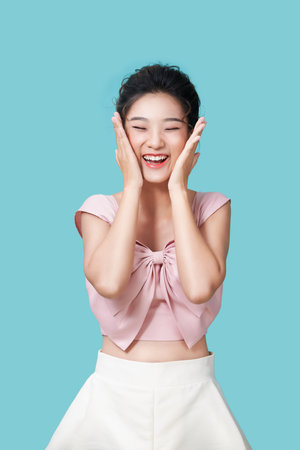 Charming lady palms near face shiny smile in dress on cyan backgroundの写真素材