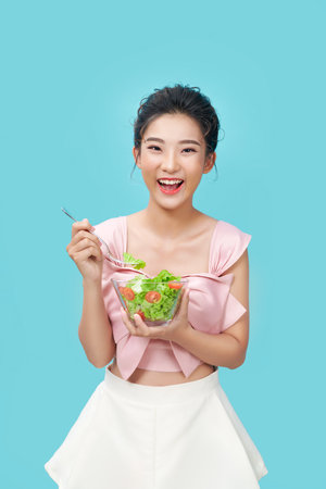 Asian young woman eatiing salad on blue background diet food conceptの写真素材