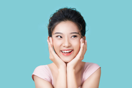 Charming lady palms near face shiny smile in dress on cyan backgroundの写真素材