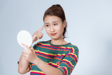 young woman looking at her wrinkles in front of the mirrorの写真素材