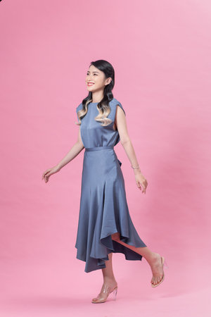 Elegant woman in blue dress and gold jewelry on pink backgroundの写真素材