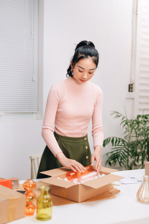 Young beautiful happy asian business woman owner of SME online using laptop receive order from customer with parcel box packaging at her startup home officeの写真素材