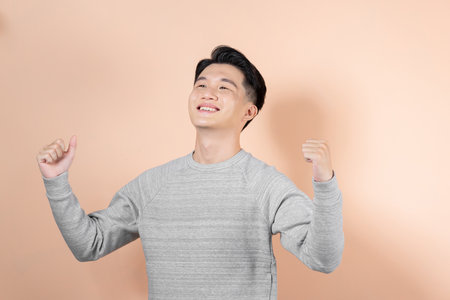 Excited young Asian man celebrating success with raised fist isolated on beige background.の写真素材
