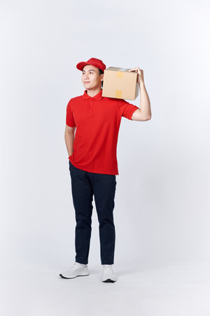 Work at post office. Courier in red uniform holding big parcel, free space, studio shotの写真素材