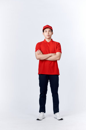 Smiling friendly-looking asian delivery guy in blue uniform cross arms and looking confident, standing white background ready to help, bring order to clientの写真素材