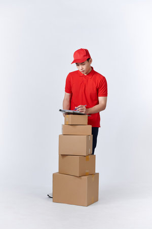 happy delivery man in red uniform holding clipboard while standing with parcel boxes nearの写真素材