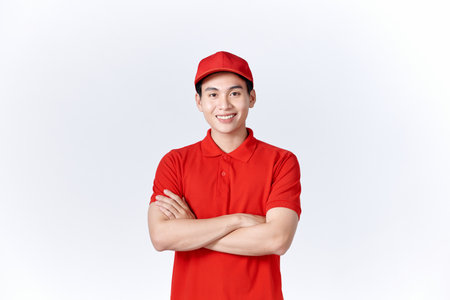Smiling delivery man in red uniform standing with arm crossed - isolated on white backgroundの写真素材