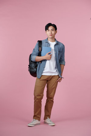 Smart guy student with backpack and bunch of books smiling at camera, copy space for advertisement over pink backgroundの写真素材