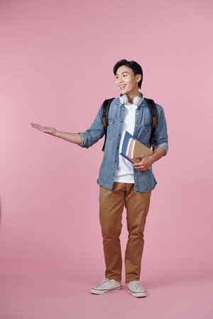 Young student man isolated on pink background extending hands to the side for inviting to comeの写真素材