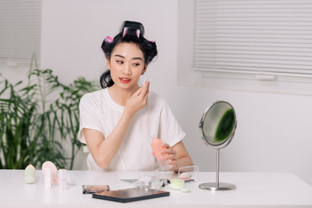 smiling young woman applying lotion to cotton disc for washing her faceの写真素材