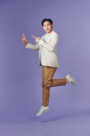 Excited casual guy pointing finger at smartphone with blank screen and jumping upの写真素材