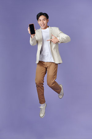 Excited casual guy pointing finger at smartphone with blank screen and jumping upの写真素材