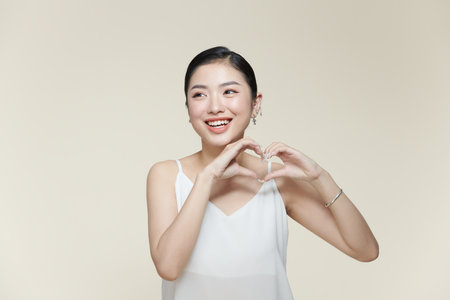 young pretty girl smiling and feeling happy, making heart shape with both handsの写真素材