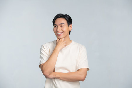 Handsome young Asian man smiling with hand on chin isolatedの写真素材