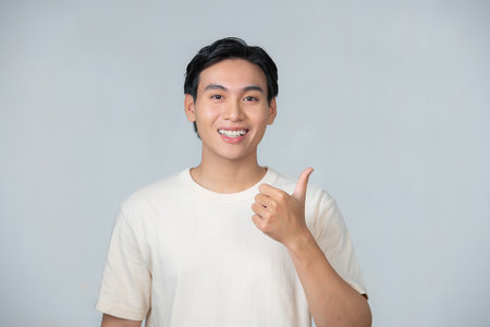 Nice smile friendly Asian man in white t-shirt giving thumbs upの写真素材