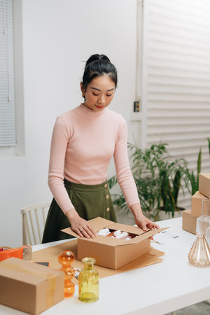 Young beautiful happy asian business woman owner of SME online using laptop receive order from customer with parcel box packaging at her startup home officeの写真素材