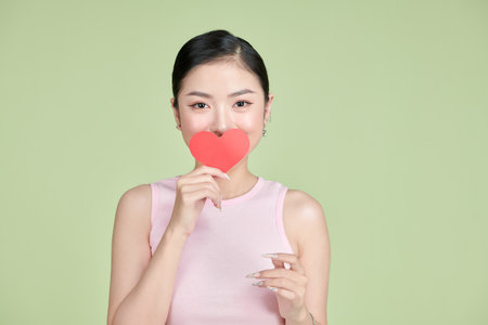 Playful Asian woman holding paper heart in front of her mouth.の写真素材