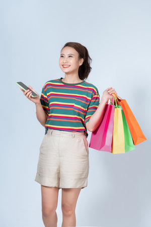 happy young woman holding shopping bags and mobile phone over white backgroundの写真素材