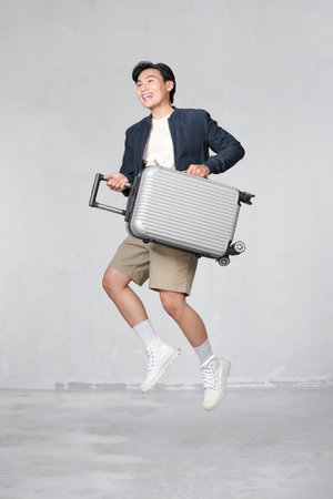 Happy Young Asian traveler man jumping with suitcase bag isolated on white backgroundの写真素材
