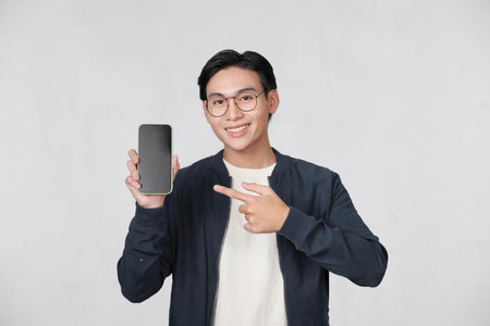 Smiling young handsome businessman pointing finger at smartphone on white backgroundの写真素材