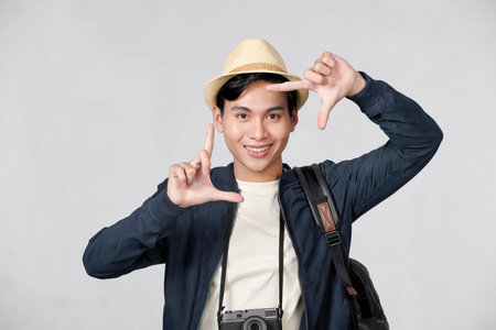 Handsome tourist young man earing backpack smiling making frame with hands and fingers with happy faceの写真素材