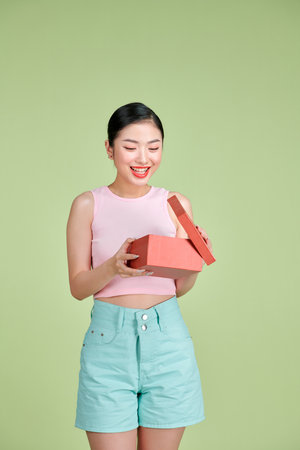 Happy young woman opening present for Valentine's Day on green studio background,の写真素材