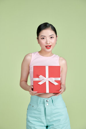 Portrait of a happy pretty asian woman holding present box while standing isolated over green pastel backgroundの写真素材