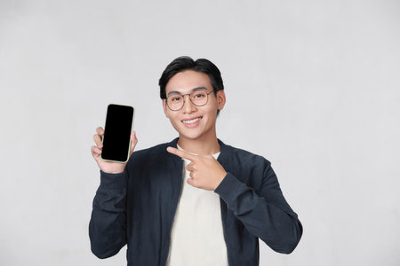 Cheerful asian guy pointing at smartphone with blank screen in his handの写真素材