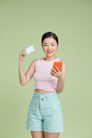 Young asian woman isolated on green background buying with the mobile with a credit cardの写真素材