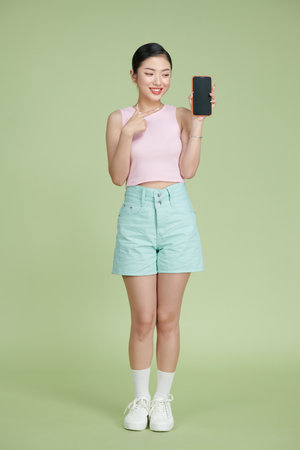 Young Asian woman holding phone in hand and pointing at it with playful expressionの写真素材