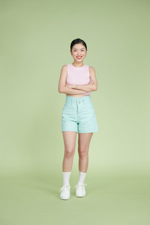 Full length of aisan woman crossed hands smiling wearing trendy clothes isolated on light green backgroundの写真素材