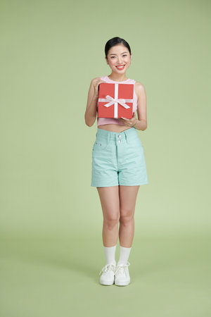 Happy woman holding gift box and looking at the camera while enjoys over green backgroundの写真素材