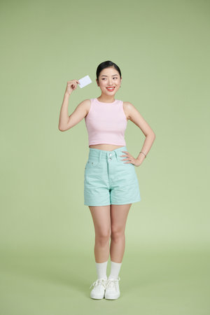 Young smiling beautiful Asian woman presenting credit card in hand showing trust and confidence for making paymentの写真素材