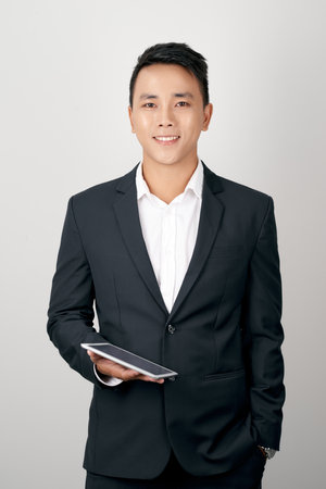 Portrait young asian business man in suit standing using tablet computer to internet isolated on white backgroundの写真素材