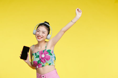 Young cheerful happy Asian woman wearing headphones listening to music from mobile phoneの写真素材
