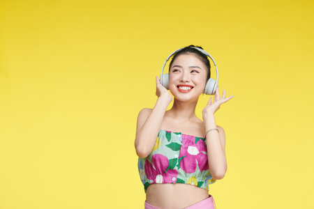 happy young woman adjusting headphones while listening music isolated on yellowの写真素材
